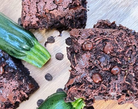 Chocolate zucchini brownies topped with chocolate chips, surrounded by fresh zucchini.