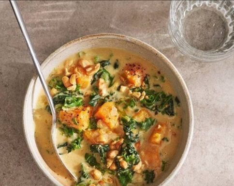 Bowl of creamy soup with greens, roasted squash, and crunchy toppings.
