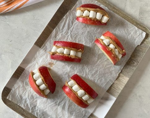 Sliced apples with marshmallow "teeth," resembling smiling mouths on a baking tray.