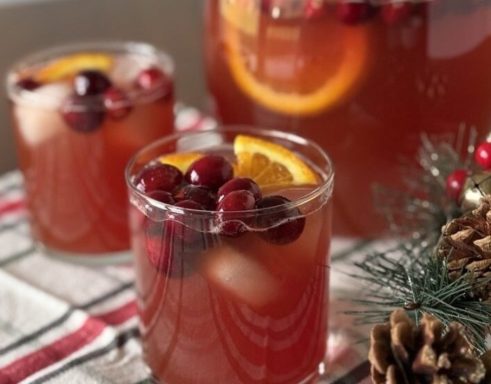Two glasses of cranberry punch with orange slices and cranberries, surrounded by festive decor.