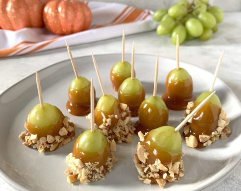 Caramel-covered grape bites topped with nuts, arranged on a white plate.