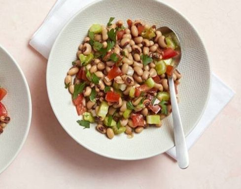 Bowl of black-eyed peas mixed with tomatoes, celery, and herbs.
