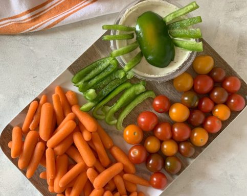 A platter with carrots, cherry tomatoes, green peppers, and a bowl of dip.