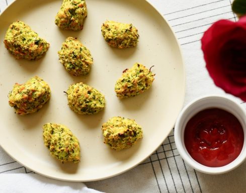 Plate of yellow-colored fritters with herbs, accompanied by a bowl of red dipping sauce.