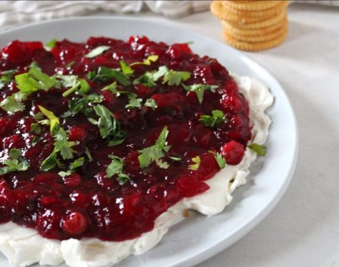 Creamy dip topped with raspberry sauce and cilantro, served with crackers on the side.