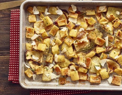 Roasted diced potatoes with herbs and cheese on a baking sheet.