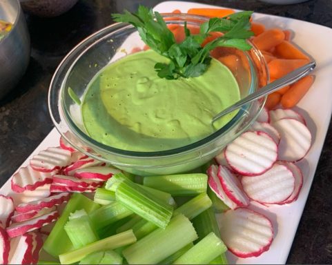 Vegetable platter with celery, carrots, radishes, and green dip garnished with parsley.